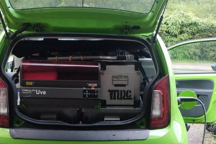 Der geöffnete Kofferraum des grünen Fahrzeugs, darin der große Lasercutter verladen