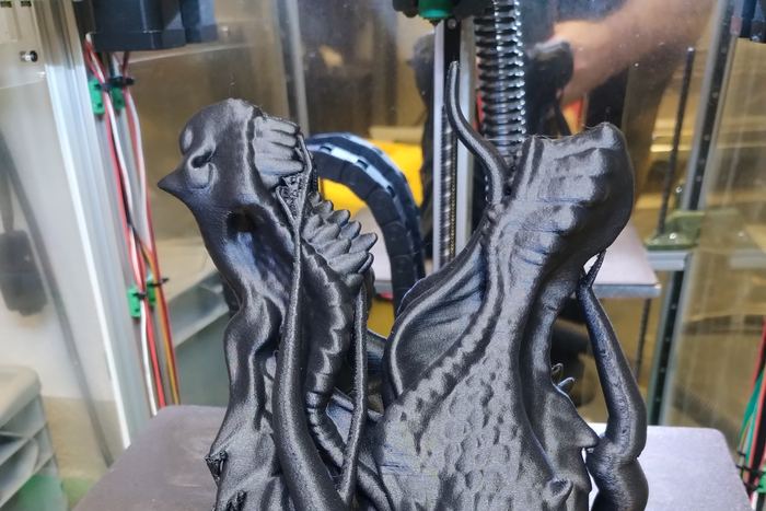 Eine schwarz gedruckte Alienfigur mit langem Schädel steht fertig auf dem Druckbett