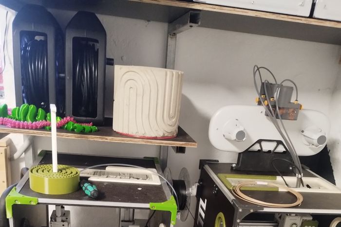 Mehrere 3D-Drucker nebeneinander, daneben frisch gedruckte Objekte