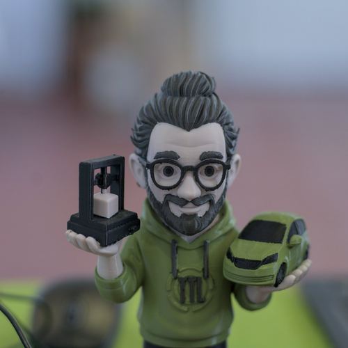 Eine 3D-gedruckte Figur von Michael Mattern hält einen winzigen 3D-Drucker und ein Modell des grünen Fahrzeugs in den Händen